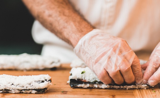 Chef de cuisine réalisant des sushis avec des gants afin de limiter la contamination bactérienne